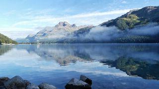 Screen split by clear reflection of mountains in lake 